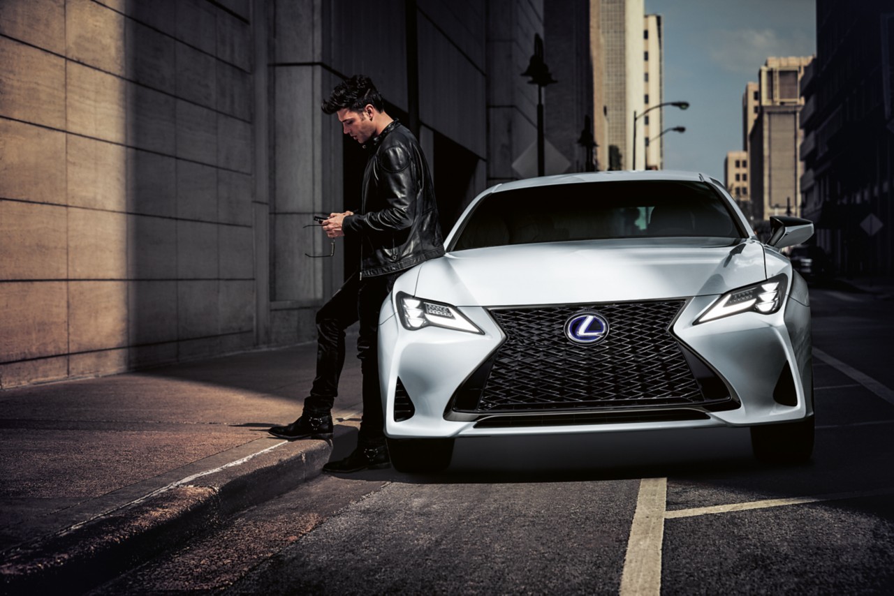 A man leaning against a parked Lexus 